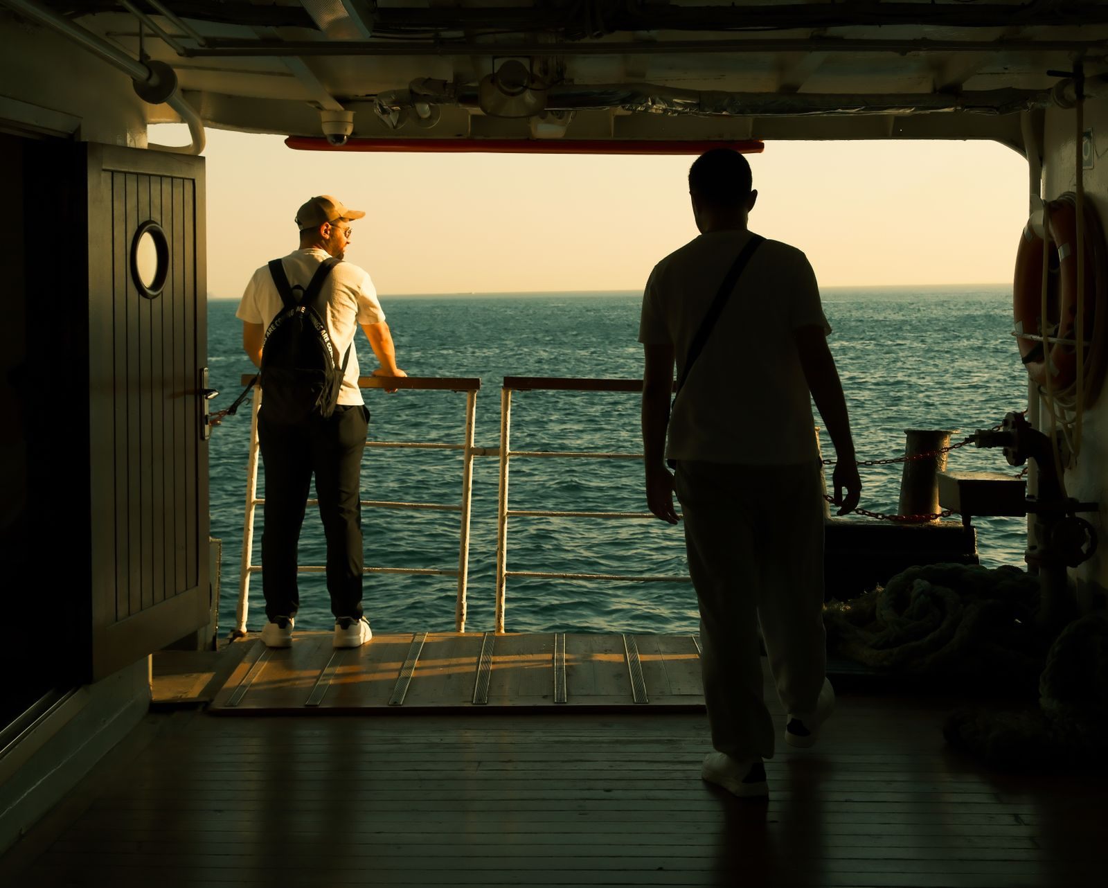 Two travelers looking out to sea from an open door on a ship