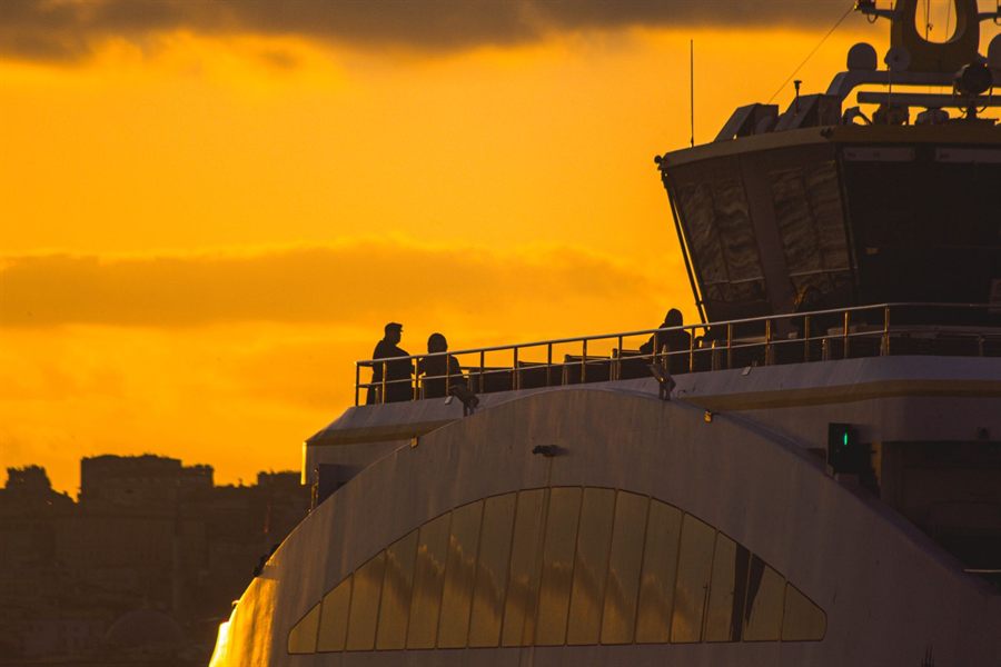 Passengers silhouetted on a ship&rsquo;s upper deck at sunset