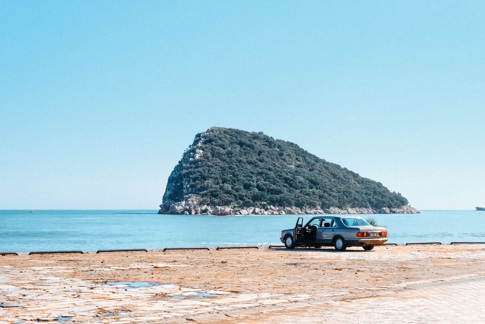 Car parked on a seaside promenade facing a green island, a drive-to habit of discount cruisers