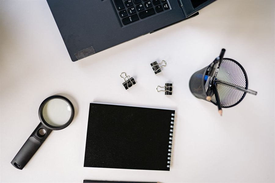 Laptop, magnifying glass and notebook on a white desk