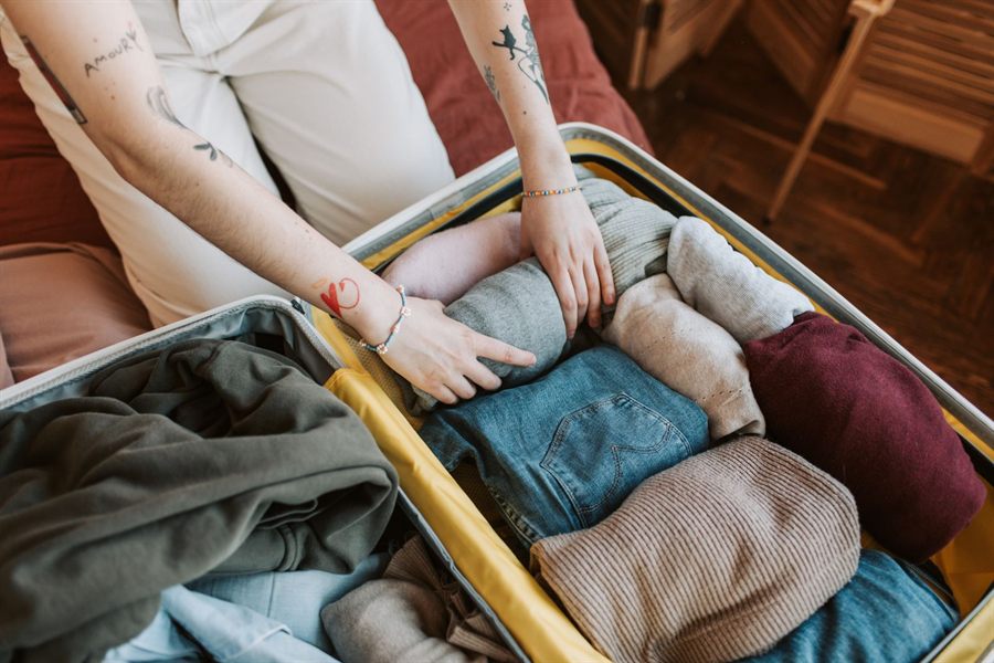 Hands packing folded clothes into a suitcase